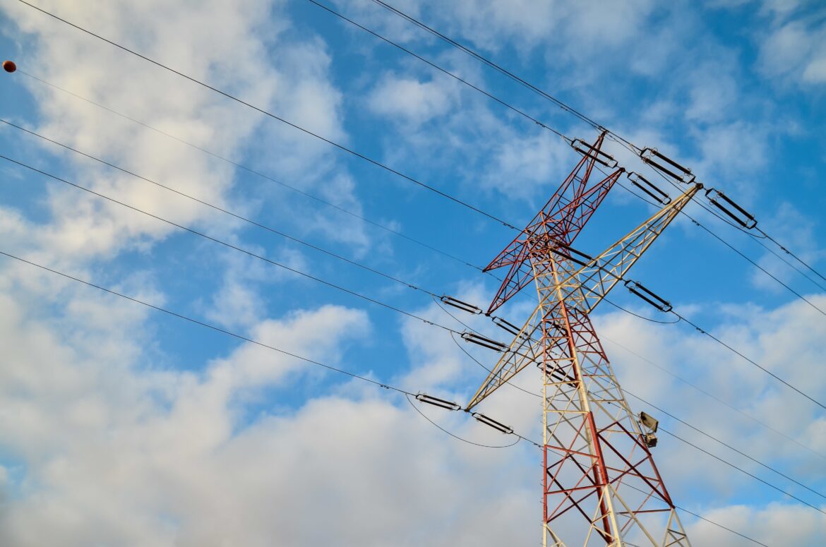 Low angle shot of a high transmission tower with a cloudy blue sky in the background